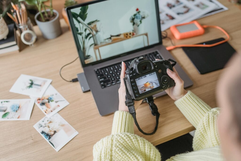 pexels-photo-7014949-7014949 Photographer adjusts camera settings while reviewing images on laptop in a creative workspace.